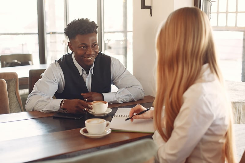 Man-talking-confidently-to-woman-who-is-taking-notes-elevator-pitch-about-yourself
