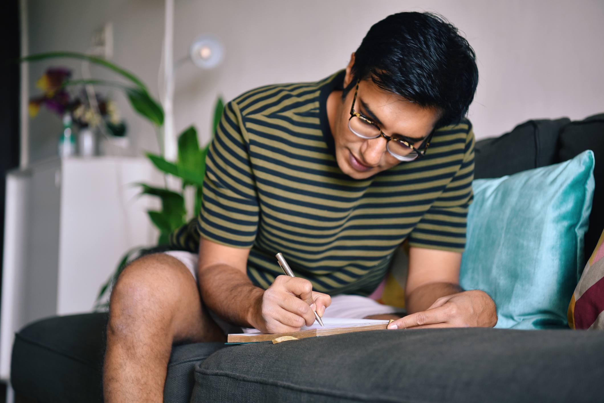 Man-writing-in-diary-on-sofa-happy-life-vs-meaningful-life