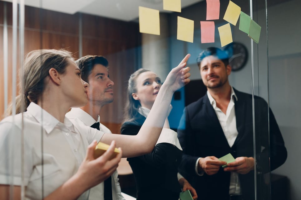 Manager-pointing-at-post-it-while-talking-to-two-coworkers-decision-making-style