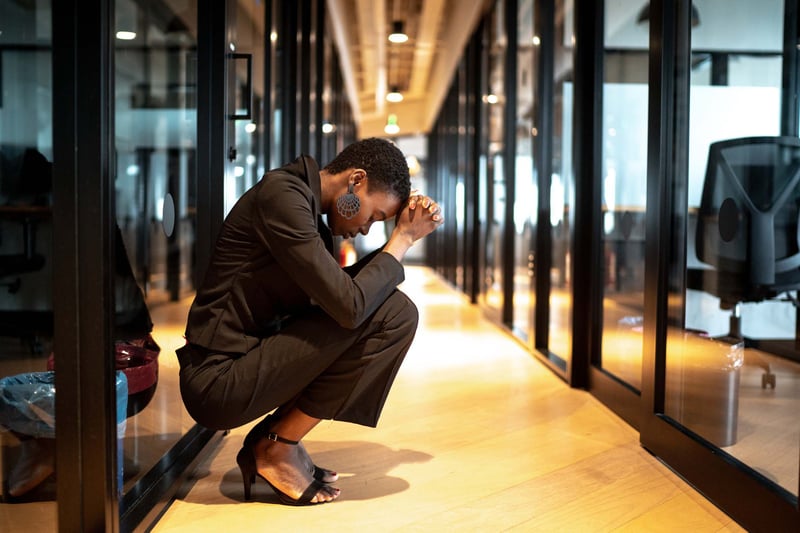 Sad-business-woman-kneeling-down-covering-her-face-at-office-hall-crying-at-work