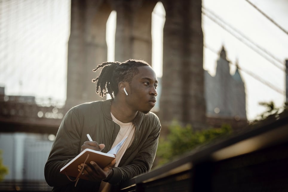 Thoughtful-man-outdoors-with-earphones-and-a-notebook-writing-things-to-manifest-ideas