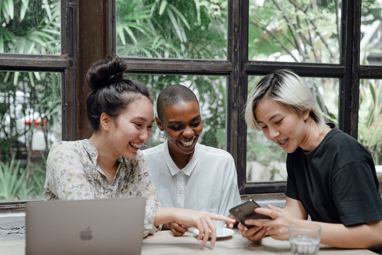 Three-women-laughing-while-talking-and-looking-at-phone-together-interview-coaching