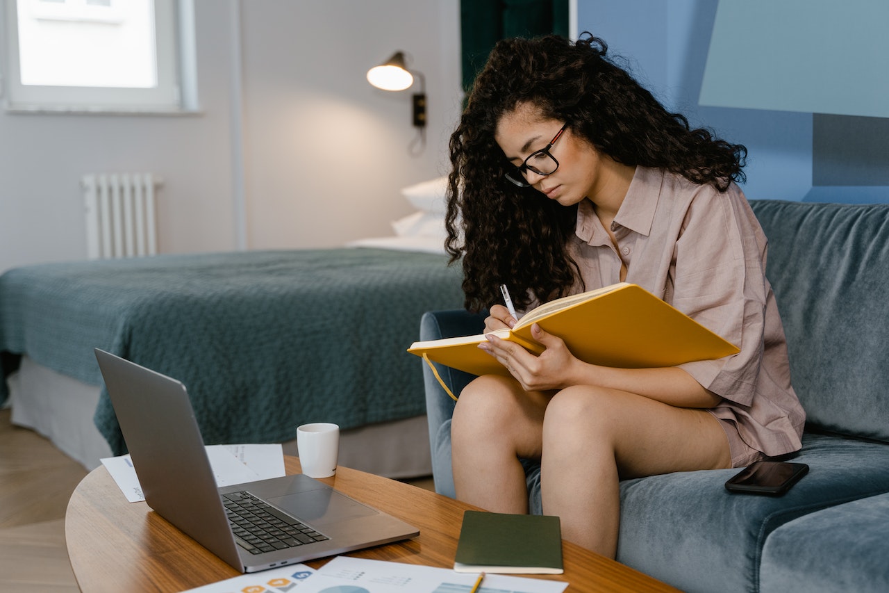 Woman-writing-on-her-notebook-at-home-with-laptop-on-the-side-elevator-pitch-about-yourself