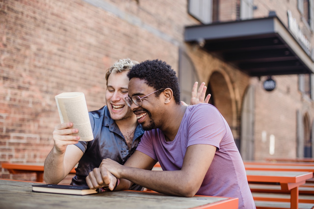 interracial-gay-couple-smiling-and-reading-book-together-outdoors-maslows-hierarchy-of-needs