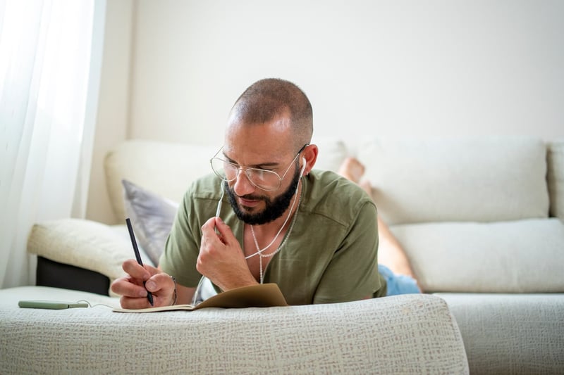 man-relaxing-lying-on-the-sofa-writing-in-his-notebook-manifestation-methods