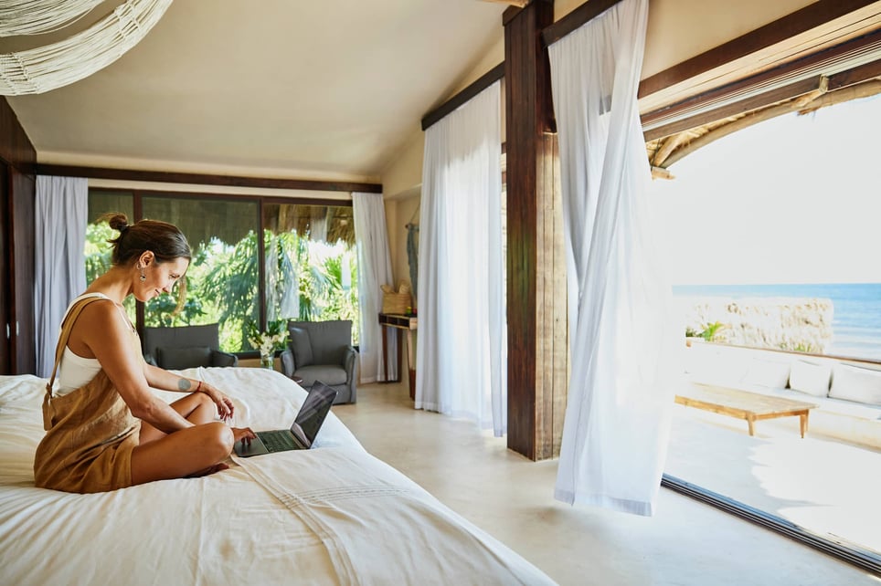 woman-working-on-laptop-while-relaxing-on-bed-in-luxury-suite-reasons-to-take-a-vacation